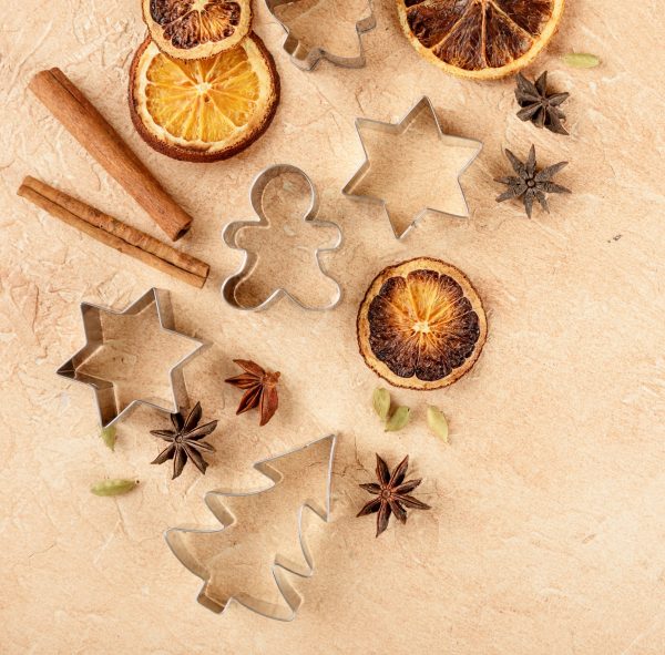 Dried orange slices, cinnamon sticks, anise stars, cardamom seeds and metal cutters for Christmas cookies on a light background