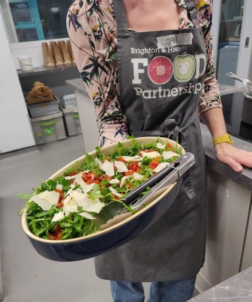 One of the community kitchens cookery teachers holds a fresh salad with rocket tomatoes and cheese