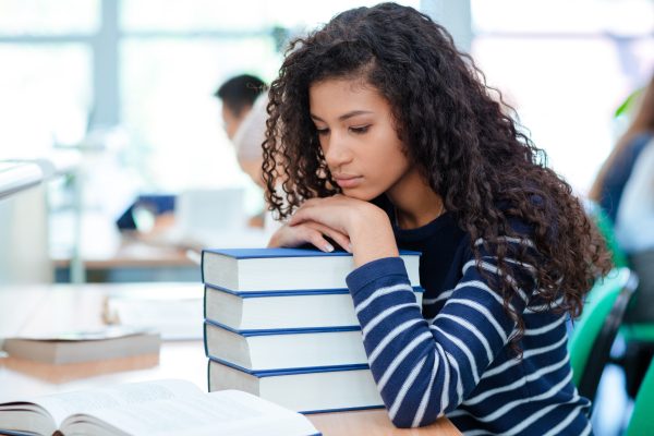 Young curly african american girl is sitting in a sad mood putting her head on books