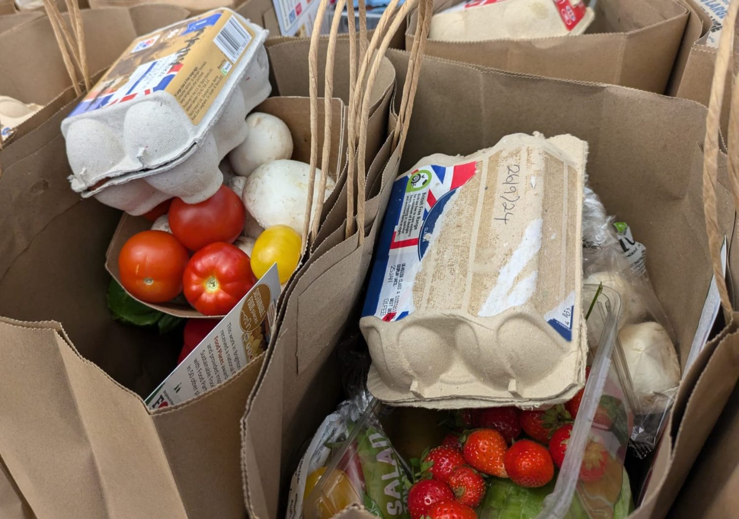 The large brown paper bags are filled to the top with local strawberries, home grown tomatoes, mushrooms, peppers, leafy greens, a box of eggs each, and more.