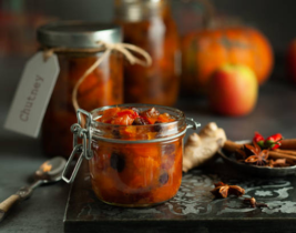 Jar of red coloured chutney without lid in forefront. Jar with red chutney in background with label reading 'chutney'